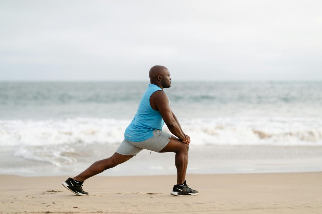 Active man in sportswear stretching on a sandy beach by the ocean.